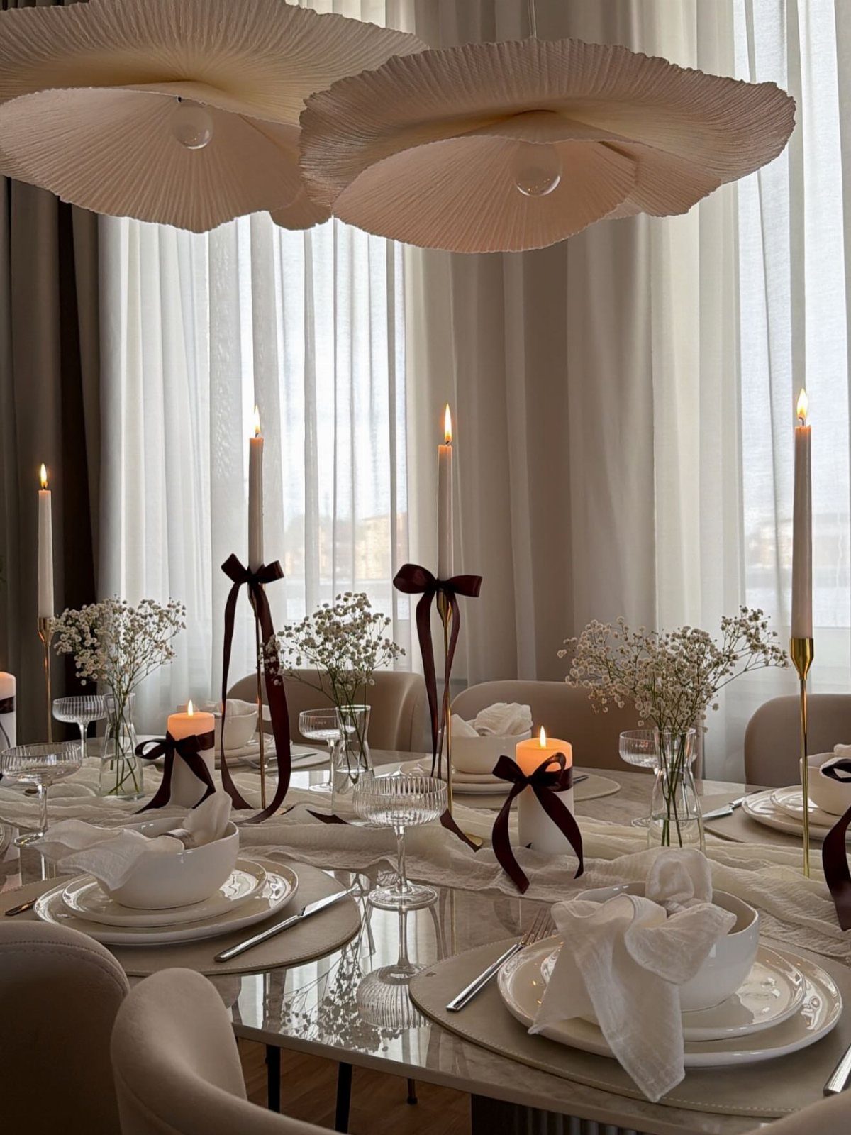 White dining table setting with white flowers, candles, and burgundy ribbon accents.