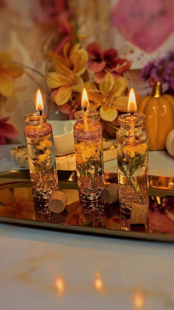 Three lit candle bottles with yellow flowers on a reflective gold tray.
