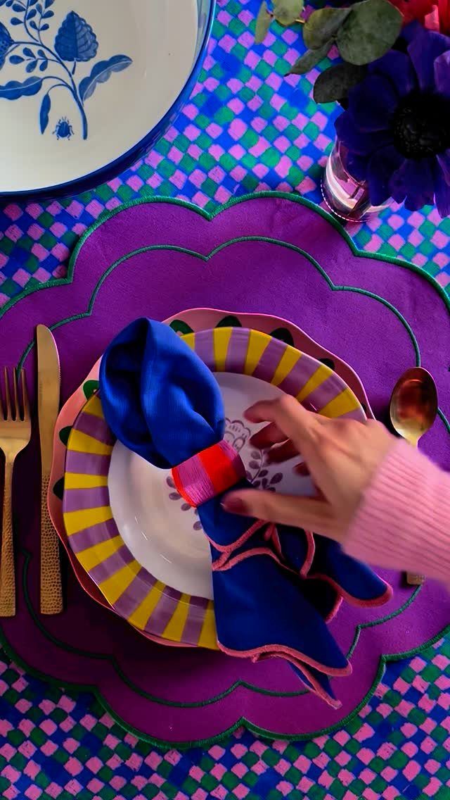 Colorful table setting with a purple placemat over a checkered tablecloth and striped plates.