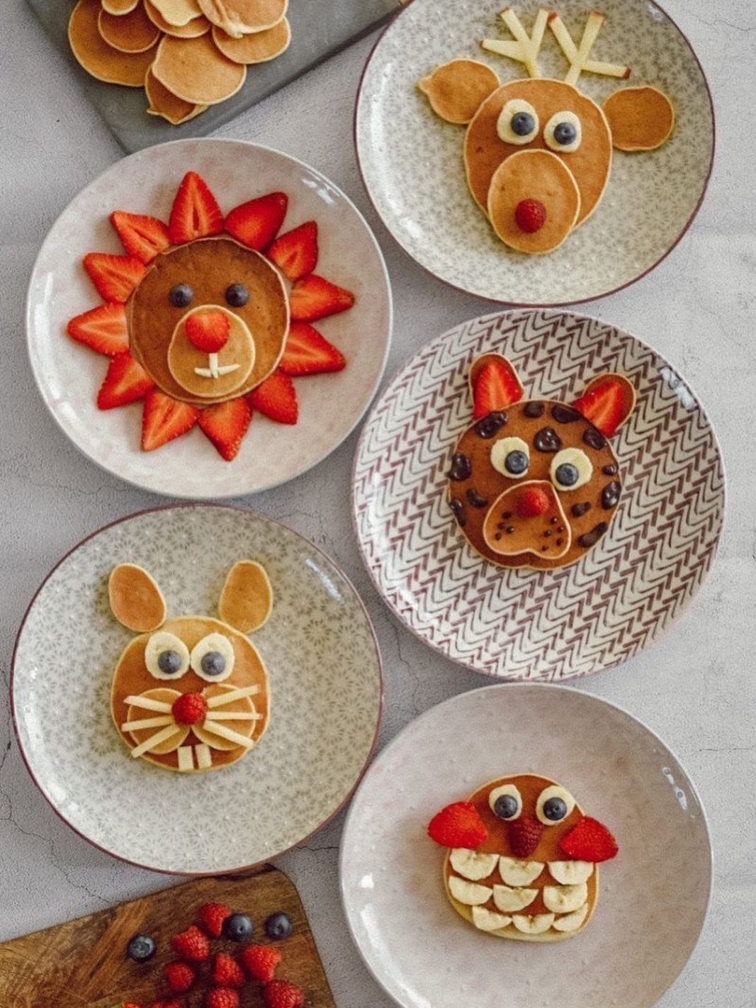 Animal-shaped pancakes decorated with fresh strawberries, blueberries, and banana slices on plates.