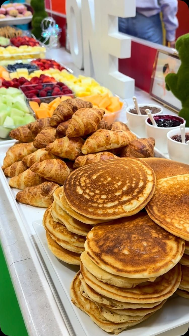 Stacks of pancakes and croissants alongside fresh fruit platters on a breakfast buffet.