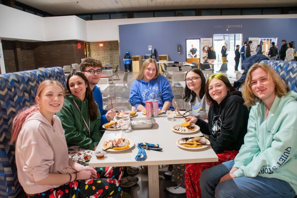 Group of young adults in pajamas eating pancakes at a white table.