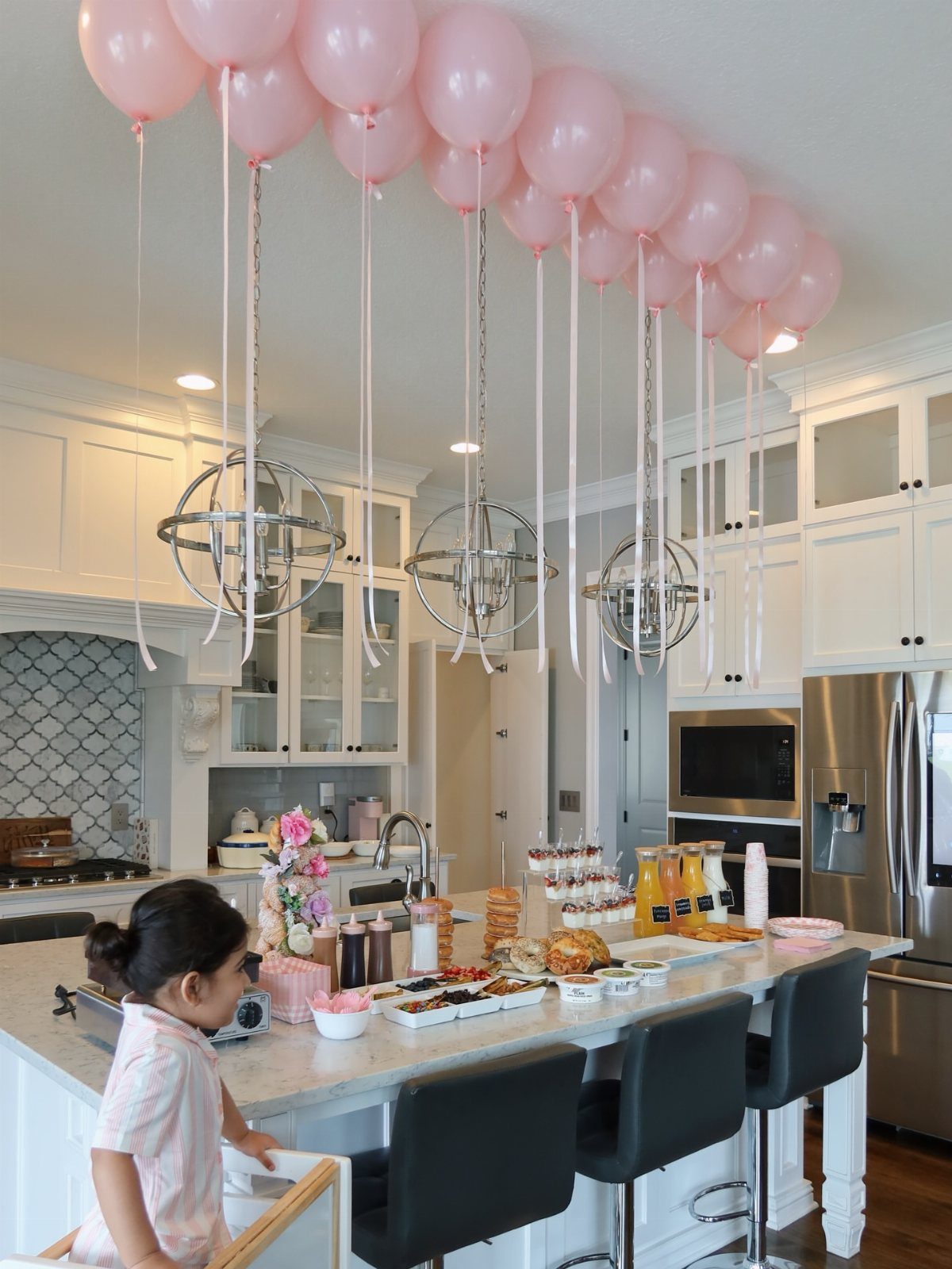 Breakfast spread on a kitchen island with pink balloons floating above.