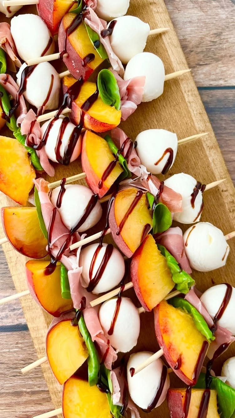 Peach and mozzarella skewers with prosciutto and balsamic glaze on a wooden board.