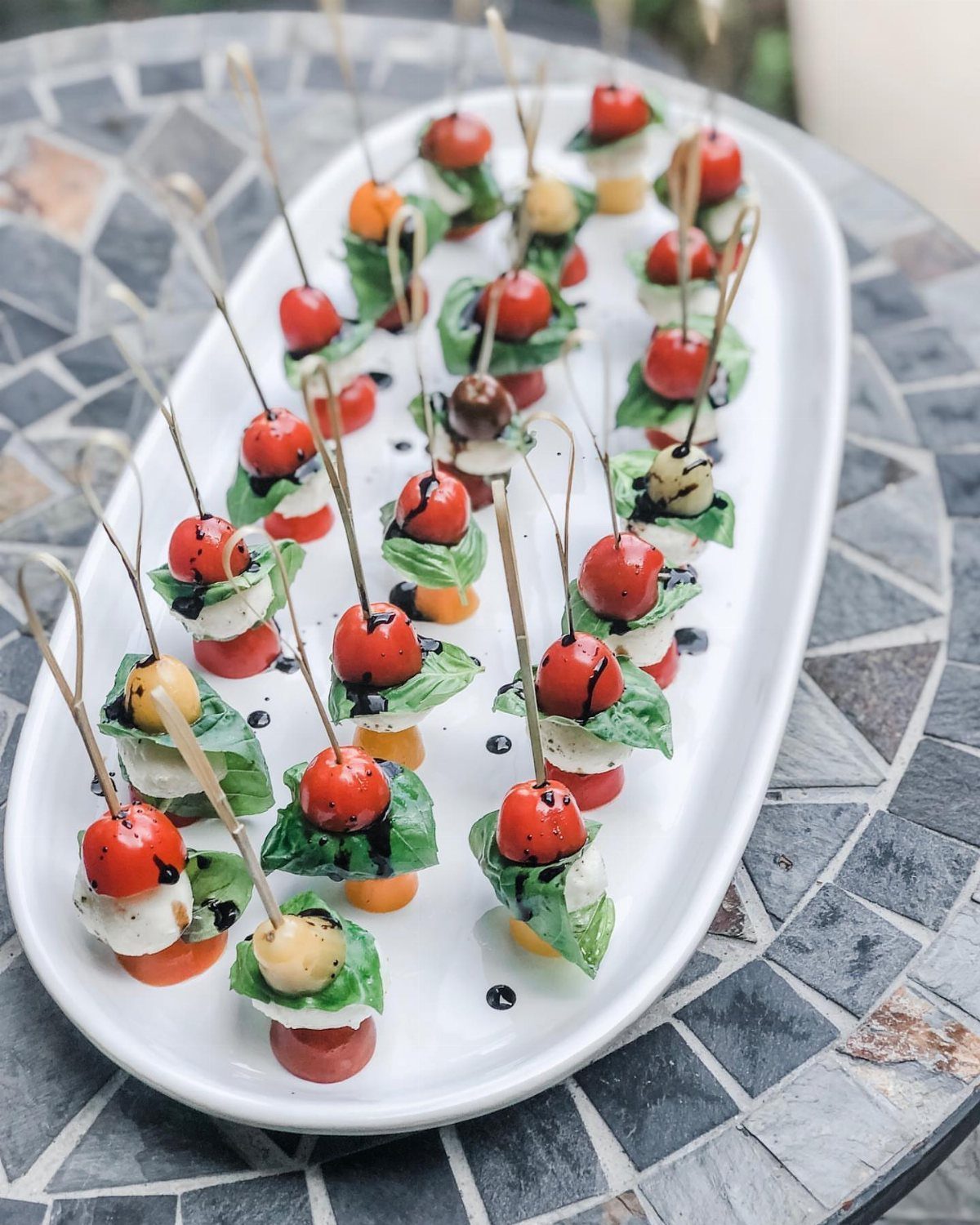 Caprese skewers with cherry tomatoes, mozzarella, and basil on a white platter.