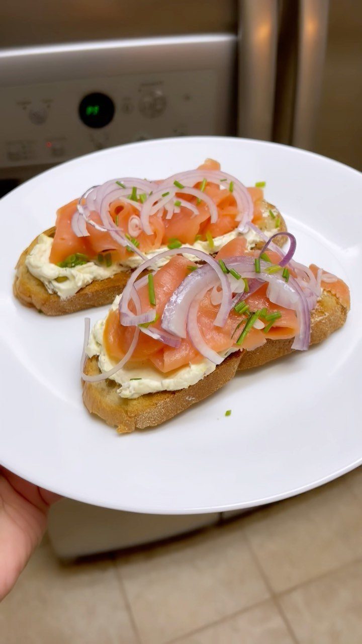 Smoked salmon toasts with cream cheese, red onion, and chives on a white plate.