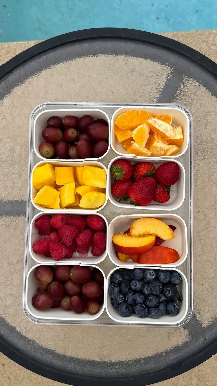 Divided white container filled with assorted fresh berries, grapes, mango, and orange slices.