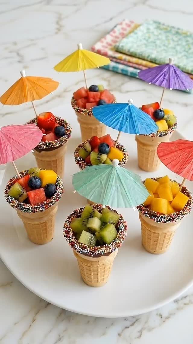 Fruit salad in chocolate-dipped waffle cones with colorful cocktail umbrellas on a plate