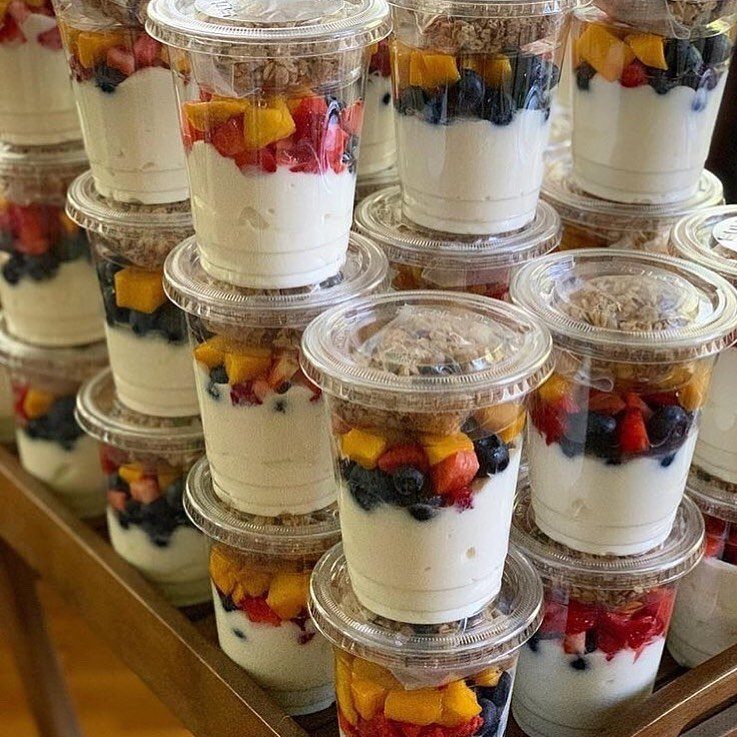 Layered yogurt parfaits with granola and fresh fruit in clear plastic cups.