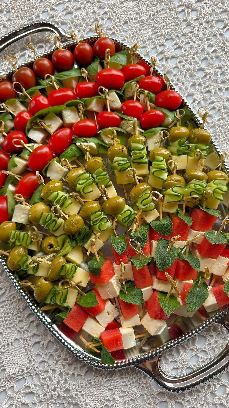 Assorted appetizer skewers with tomato, olive, and watermelon on a silver platter.