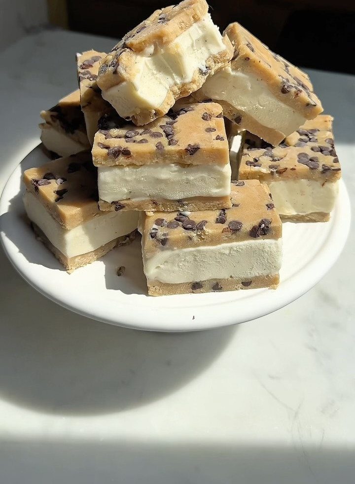 Ice cream sandwiches with chocolate chip cookies stacked on a white plate.