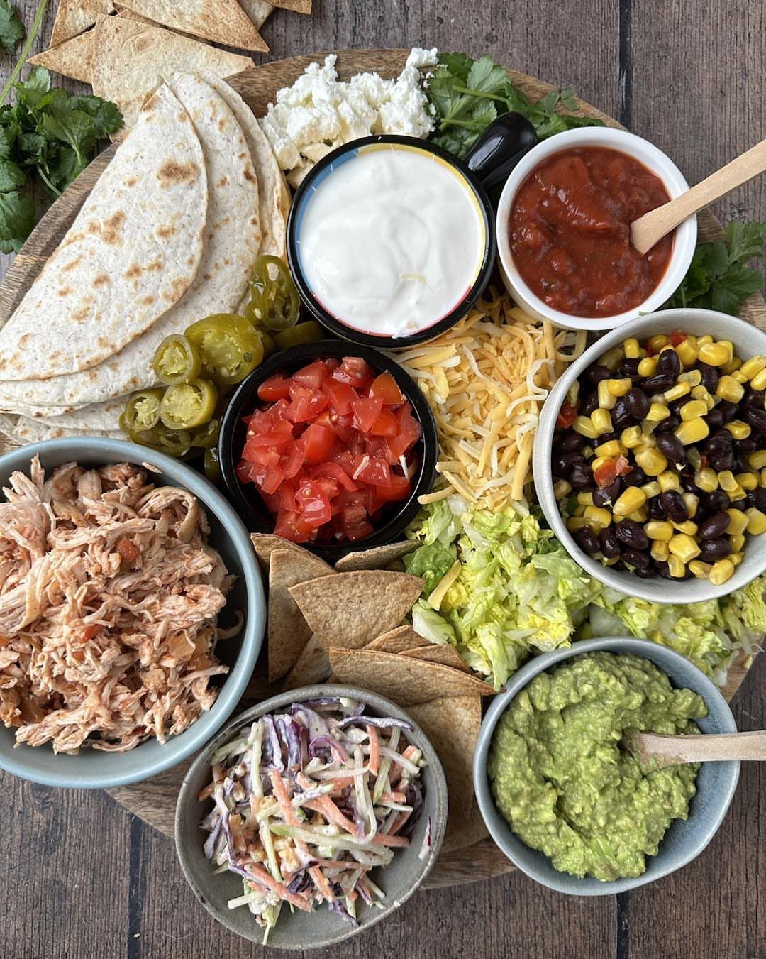 Taco platter with shredded chicken, guacamole, salsa, corn salad, and warm tortillas.