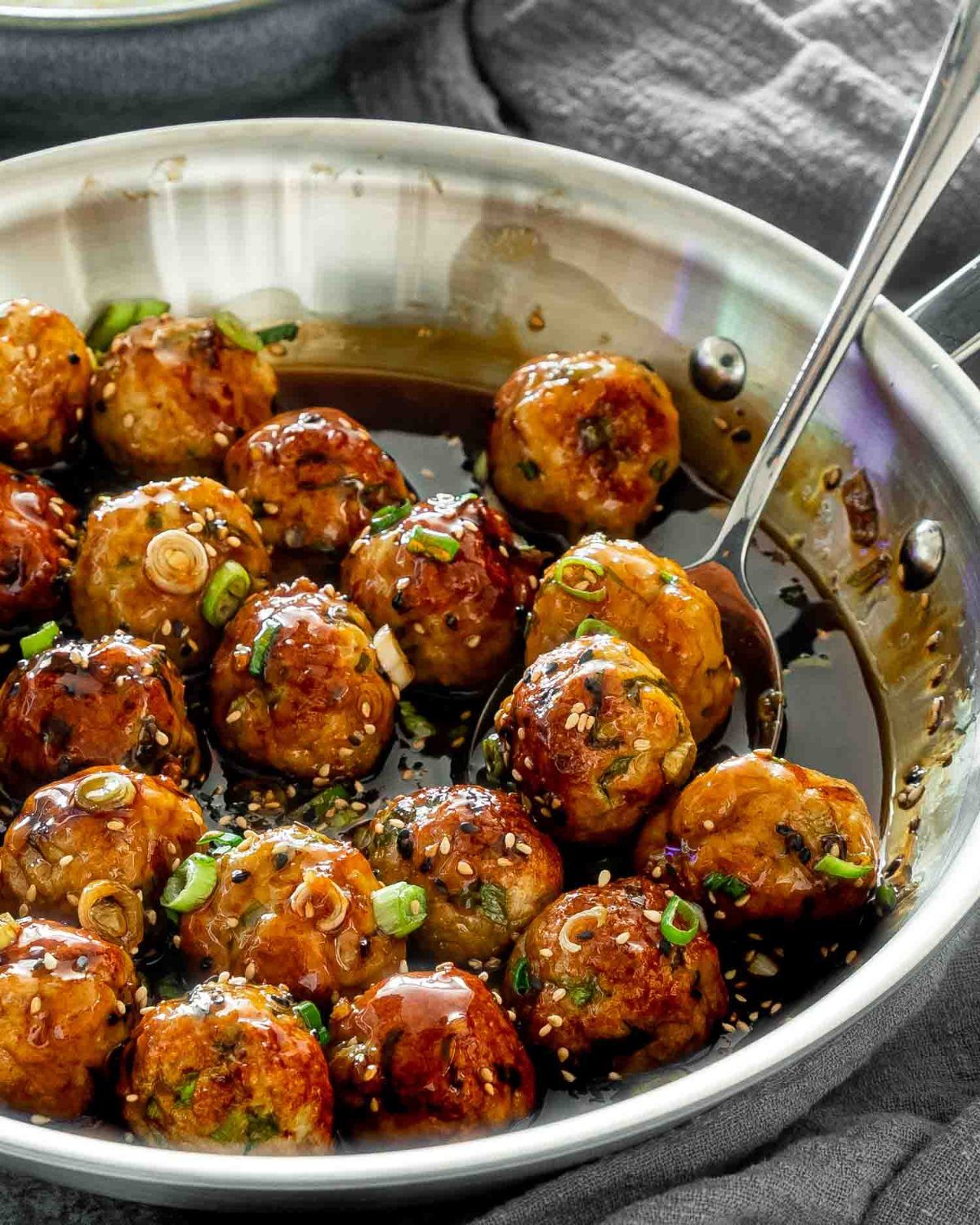 Glazed meatballs with sesame seeds and green onions in a silver frying pan.