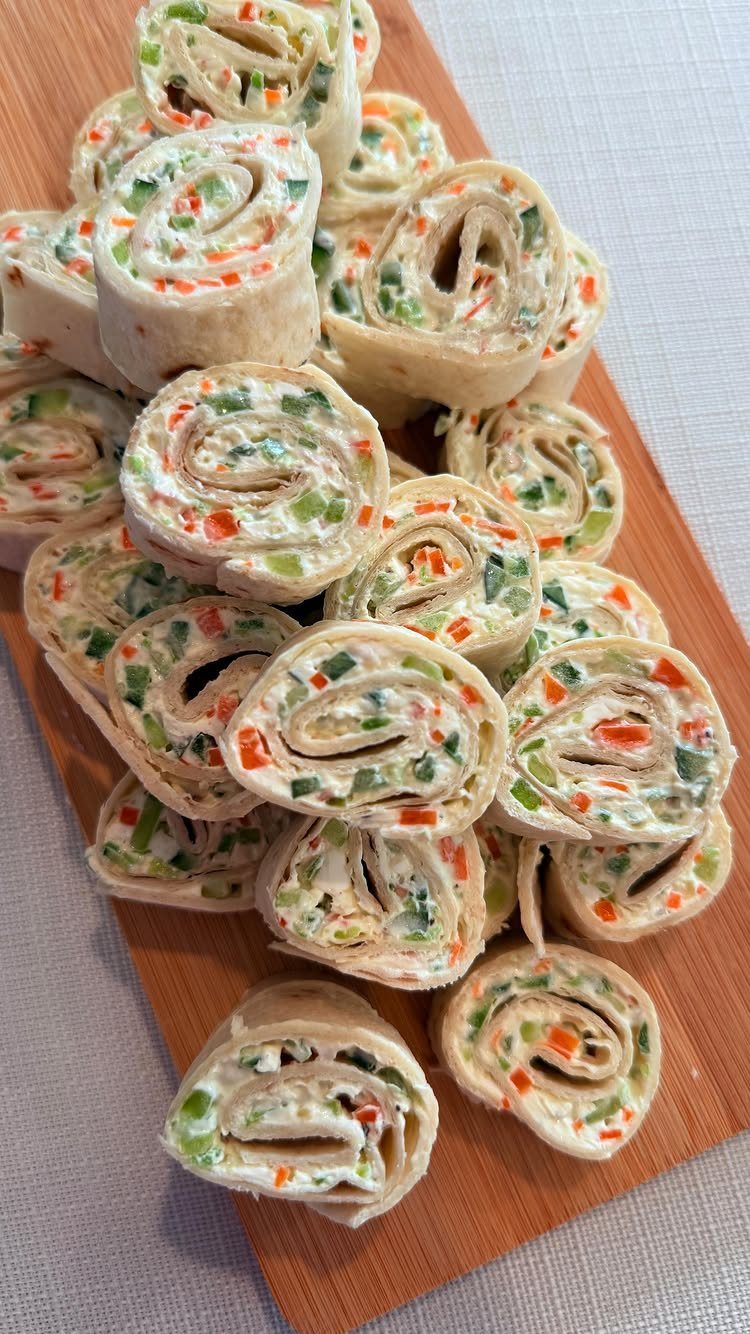 Veggie pinwheels with cream cheese and diced peppers on a wooden board.