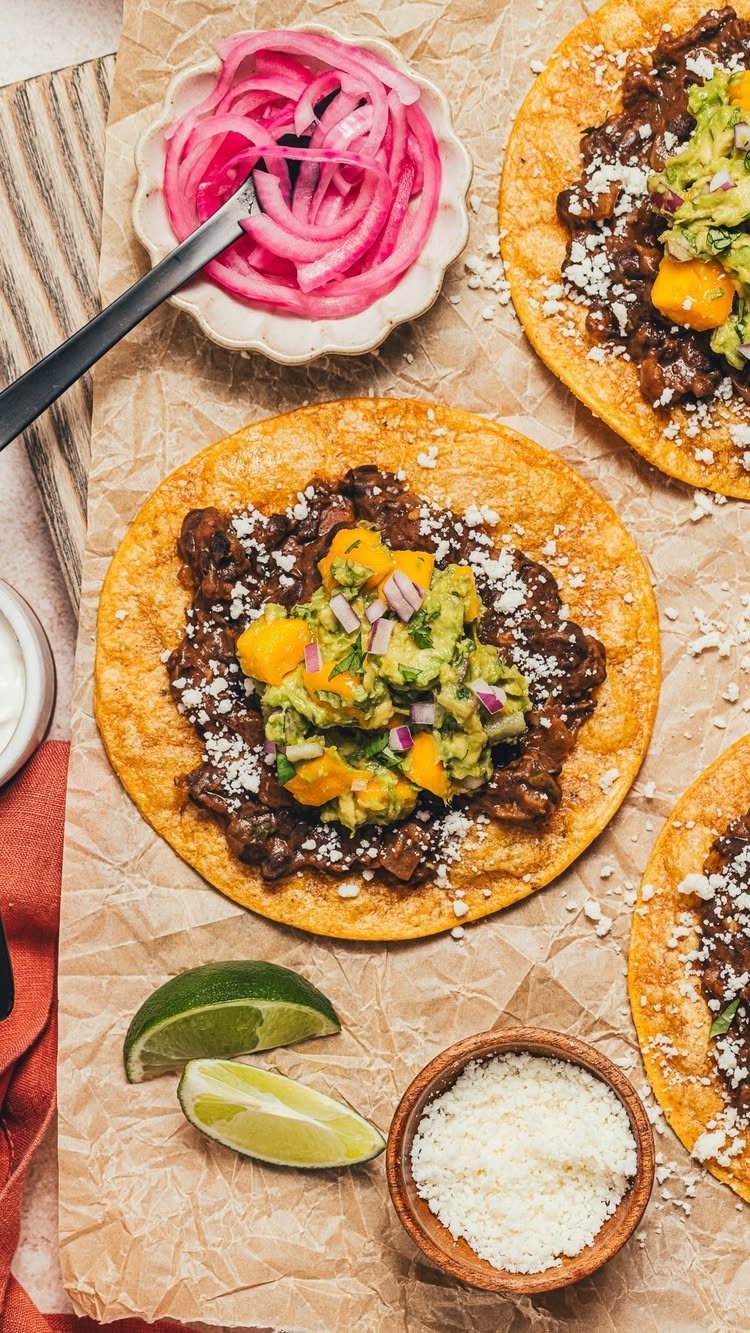 Black bean tostadas topped with guacamole and mango on brown parchment paper.