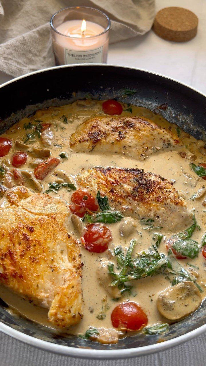 Seared chicken breasts in a creamy sauce with tomatoes and spinach in a skillet.