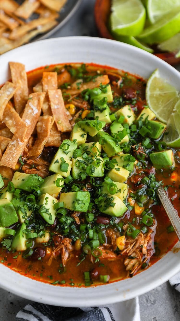 Chicken tortilla soup topped with avocado, green onions, and crispy tortilla strips.