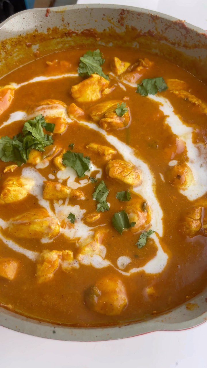 Orange chicken curry with cream swirls and cilantro in a grey skillet