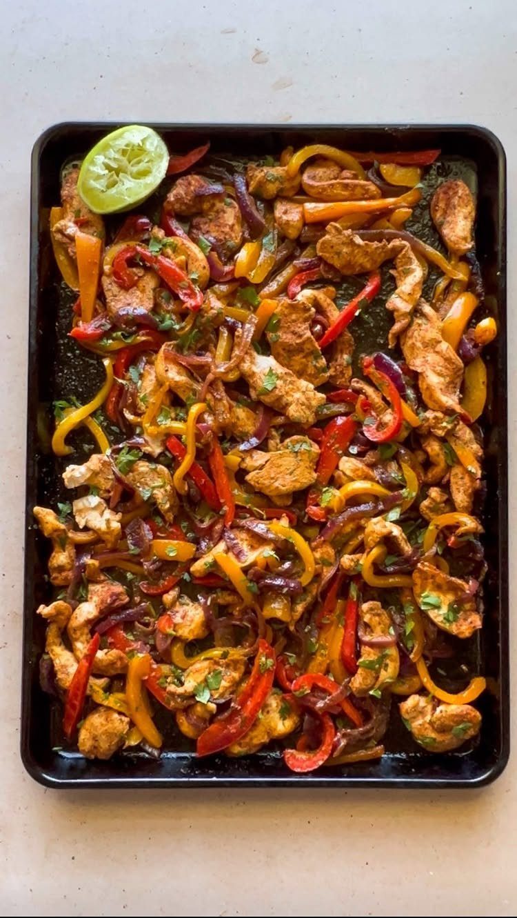 Seasoned chicken strips and colorful bell peppers roasted on a black sheet pan.