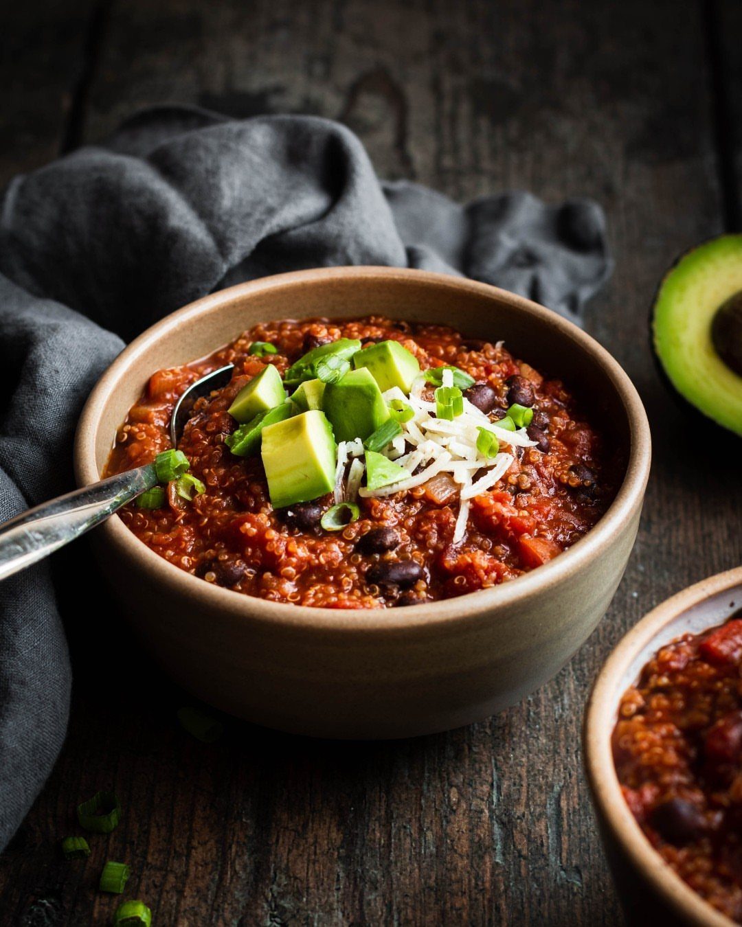 Red bean chili topped with avocado and cheese in a tan ceramic bowl.