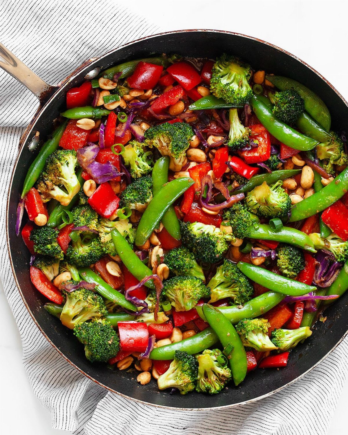 Vegetable stir fry with broccoli, red peppers, and snap peas in a black skillet.