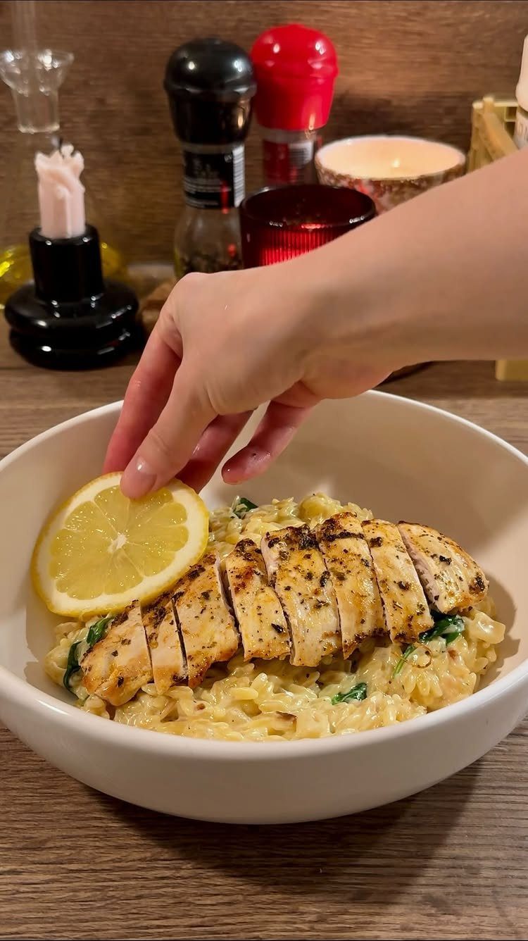 Grilled chicken breast over creamy lemon orzo with spinach in a white bowl