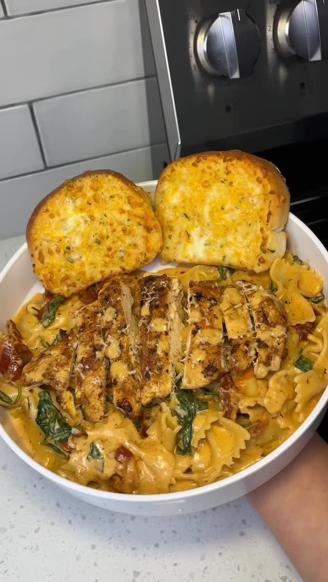 Sliced grilled chicken on creamy pasta with sun-dried tomatoes and toasted garlic bread.