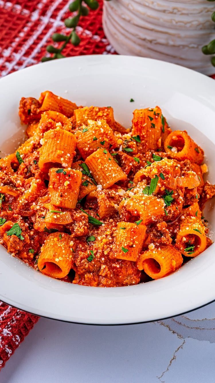 Rigatoni pasta with bolognese meat sauce, parmesan cheese, and parsley in a white bowl.