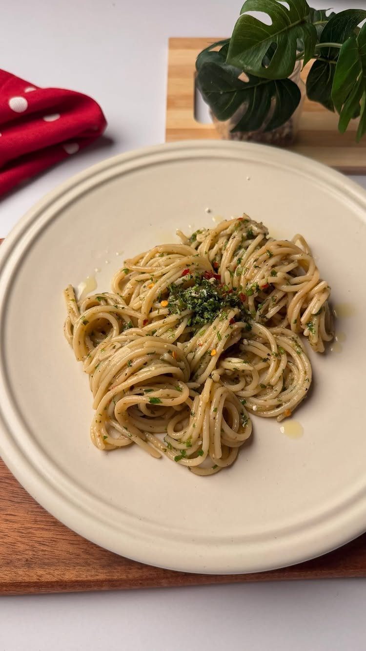 Spaghetti with garlic, oil, and herbs on a cream plate over wooden board.