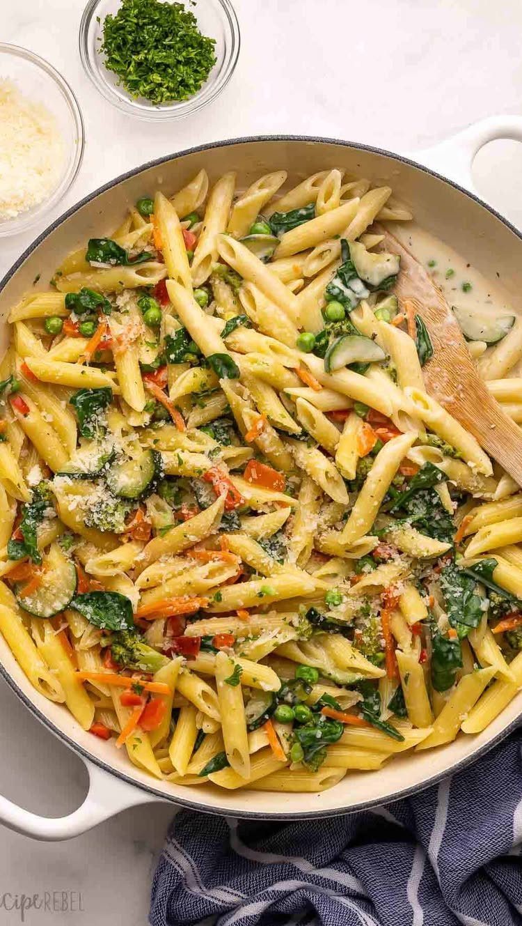 Penne pasta with mixed seasonal vegetables in a white skillet on marble.