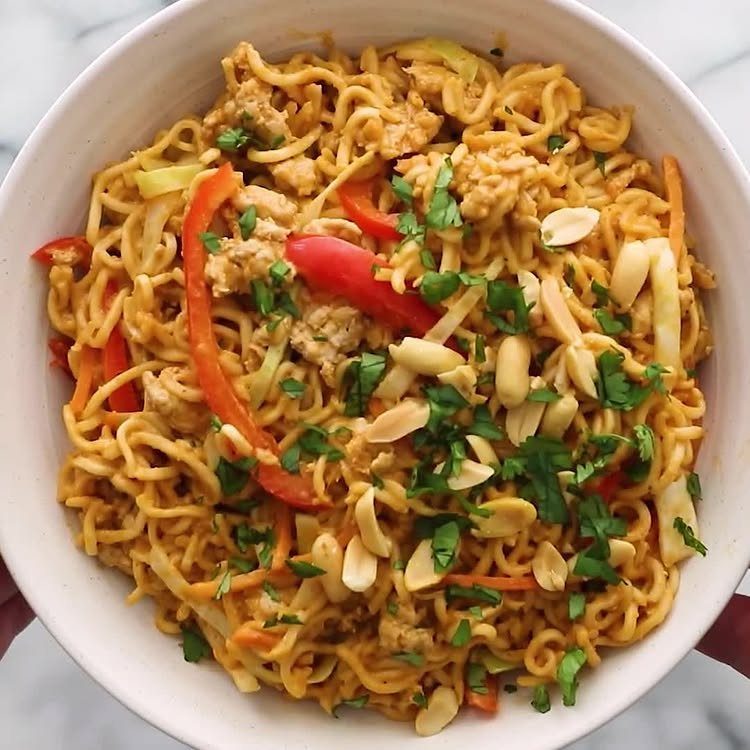 Peanut noodles with red peppers, ground meat, and peanuts in a white bowl.