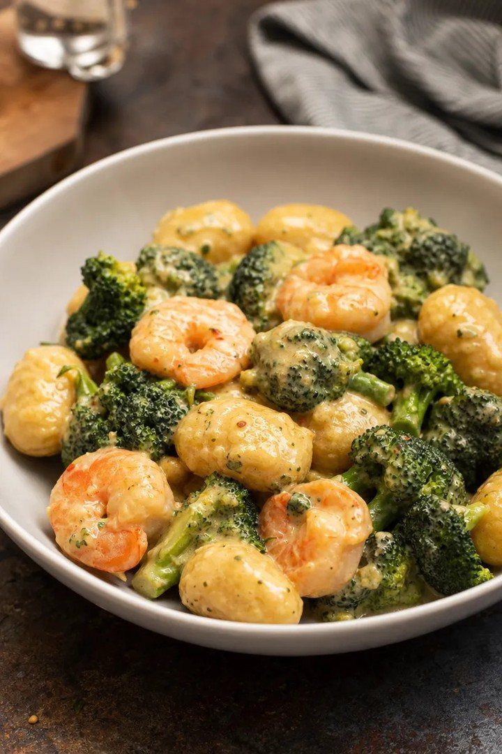 Creamy gnocchi with shrimp and broccoli served in a shallow white bowl.