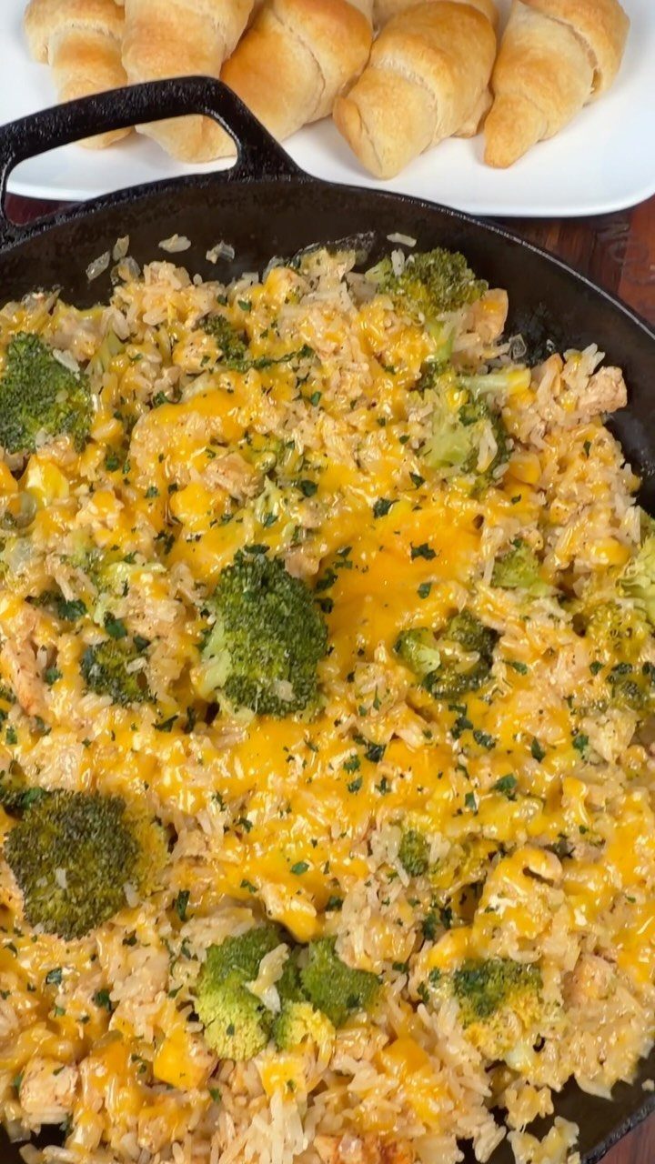 Broccoli and cheddar rice in a cast iron skillet with crescent rolls nearby.