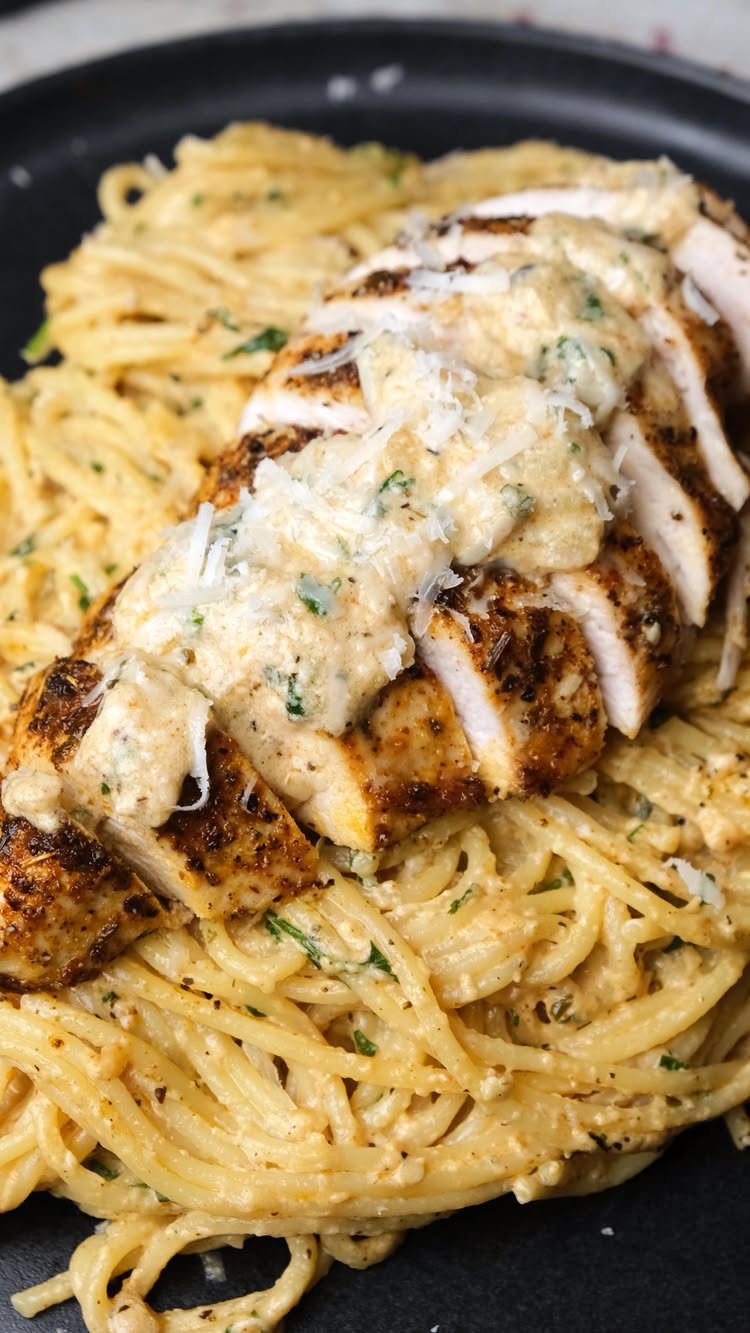 Sliced seasoned chicken breast with creamy sauce over a bed of creamy pasta.
