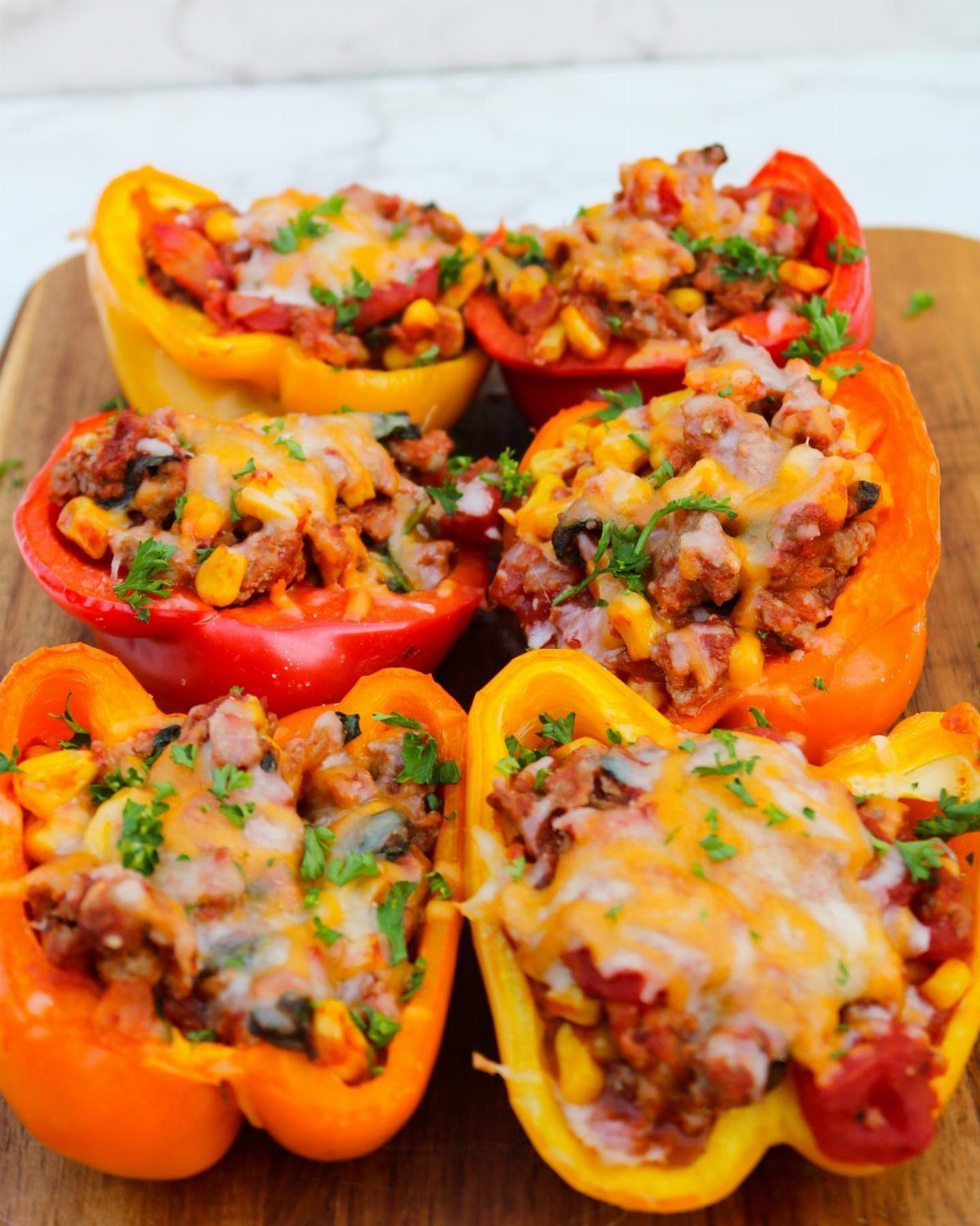 Stuffed bell peppers filled with meat, corn, and melted cheese on a wooden board.
