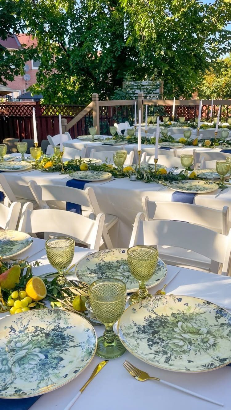 Outdoor dining tables featuring a greenery garland with white taper candles and lemons.