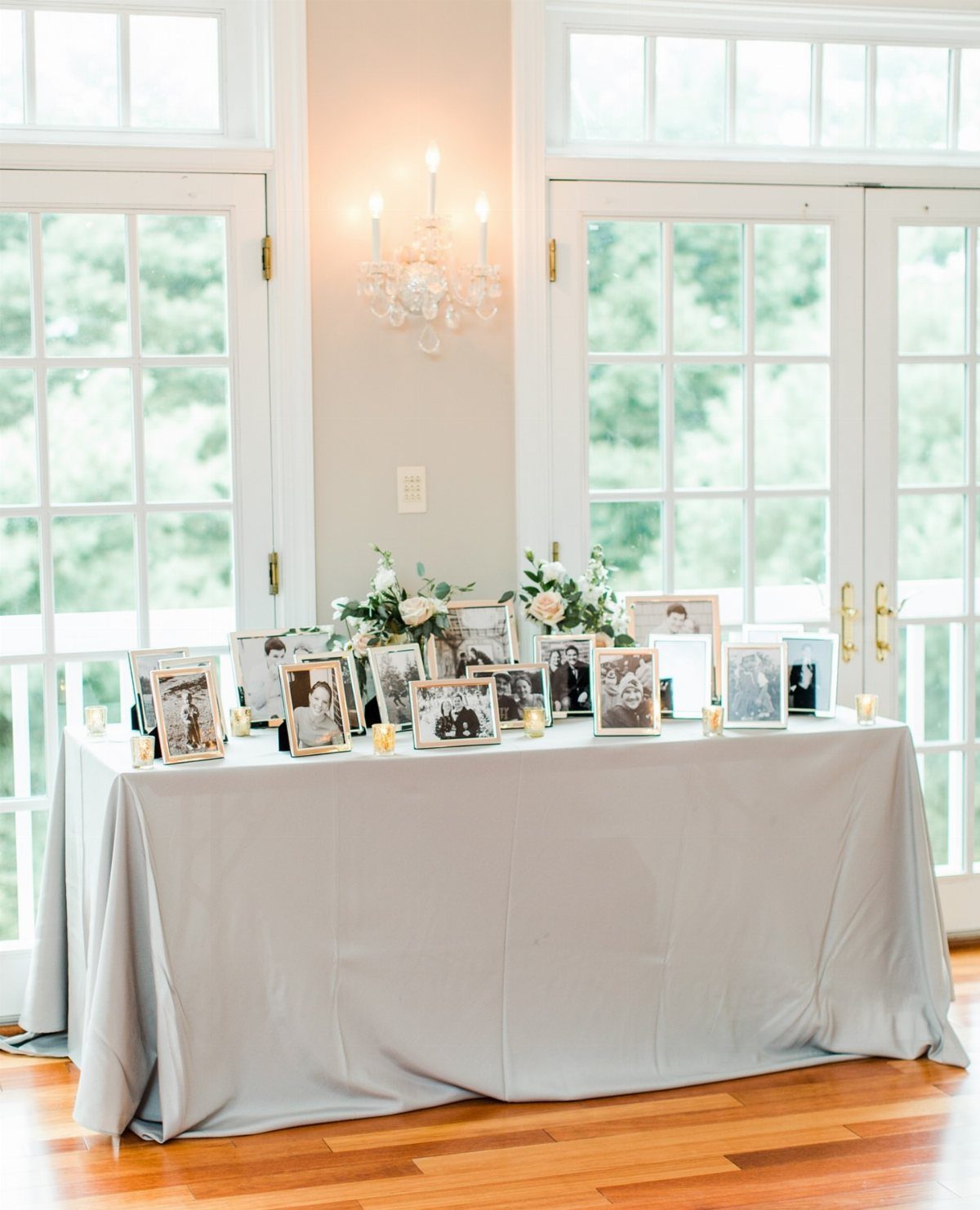 Framed black and white photographs and white flowers on a grey draped table.