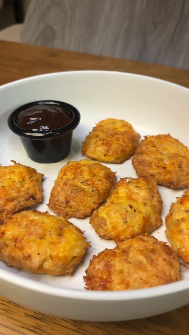 Golden-brown chicken nuggets in a white bowl with a side of dipping sauce.