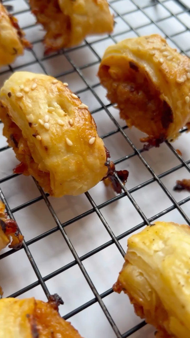 Golden-brown puff pastry rolls with sesame seeds on a black wire cooling rack.