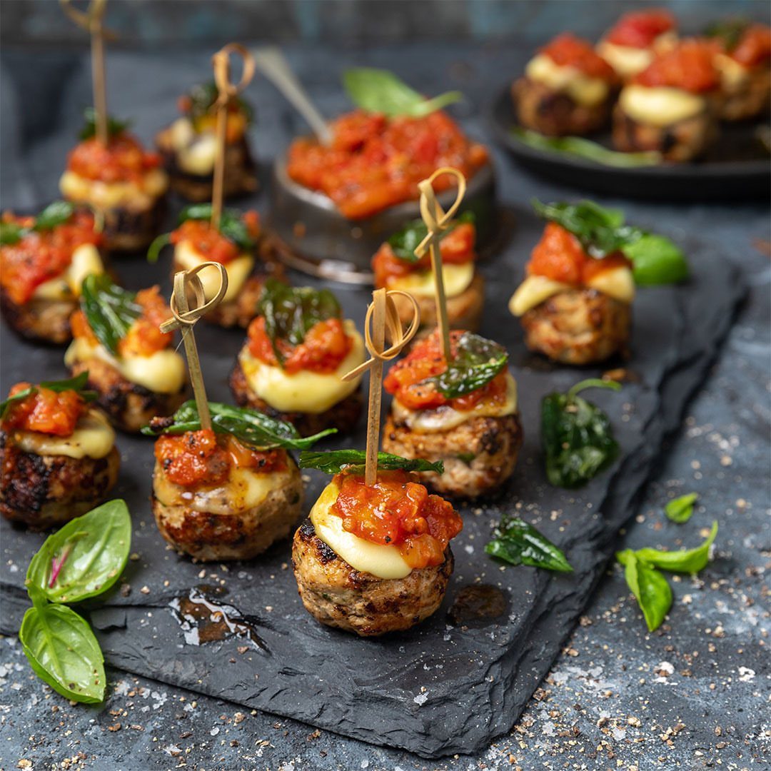 Meatballs topped with melted cheese and tomato sauce on a dark slate platter