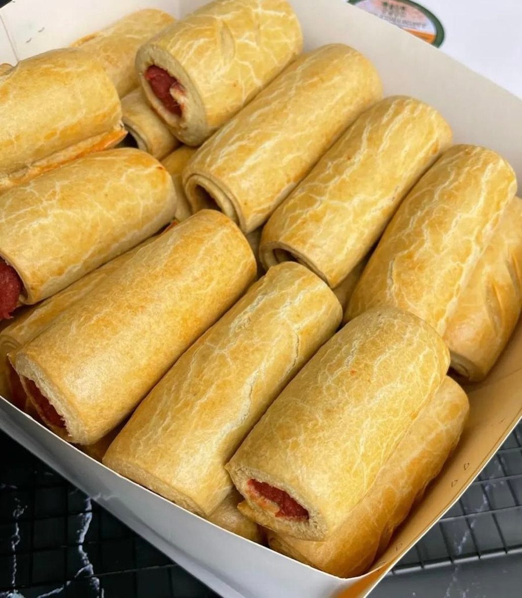 Mini sausage rolls with golden flaky pastry arranged in a white cardboard box.