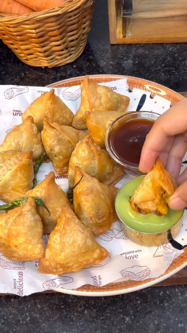 Golden-brown fried samosas on a plate with red and green dipping sauces.