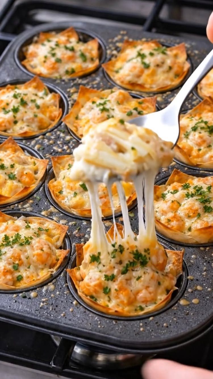 Shrimp tartlets with melted cheese and parsley in a black muffin tin.