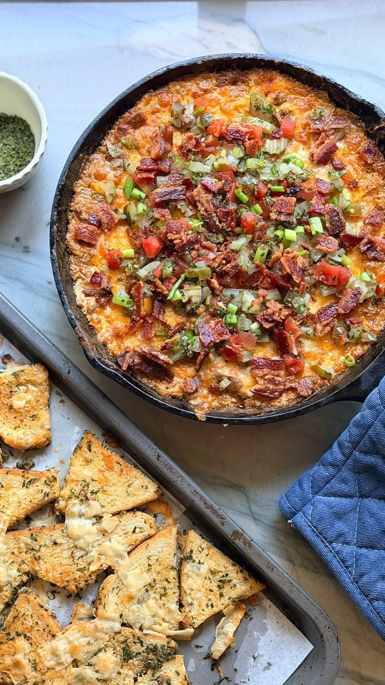 Cheesy dip with bacon and vegetables in a skillet with toasted pita chips.