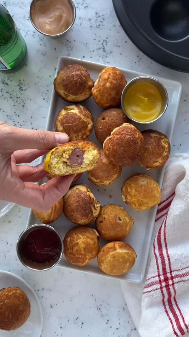 Mini corn dogs on a white platter with dipping sauces and one held aloft.