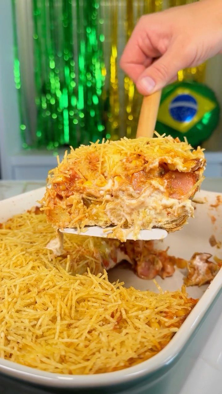 Layered casserole topped with potato sticks being lifted from a white baking dish.