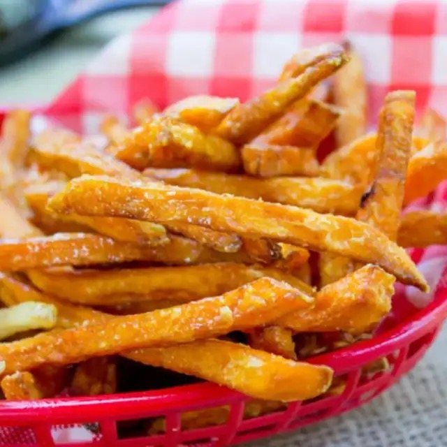 Sweet potato fries in a red plastic basket on a checkered cloth.
