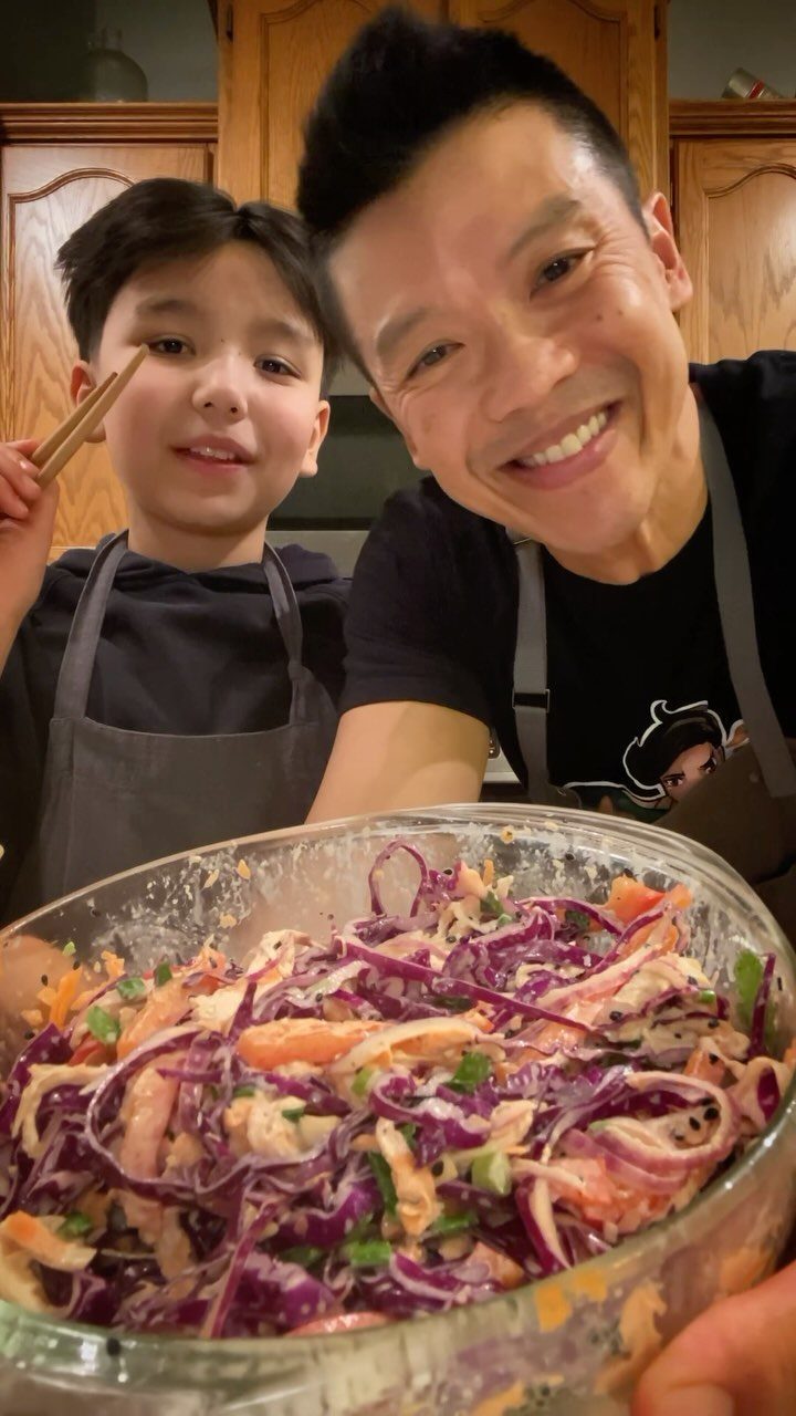 Man and boy smiling behind a bowl of chicken and purple cabbage salad.