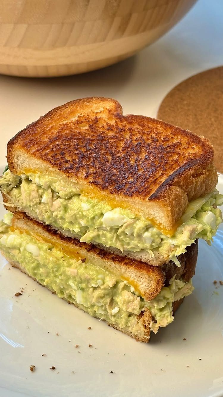 Toasted avocado tuna melts stacked on a white plate with a wooden bowl.