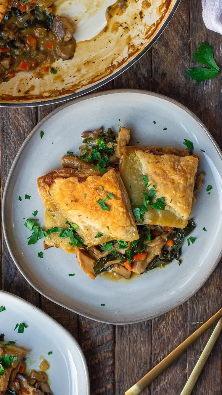 Pastry squares over creamy chicken, kale, and mushroom stew on a white plate.